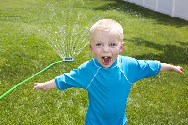 Kisfiú játszik a háztáji sprink­lerek­ — Stock Fotó