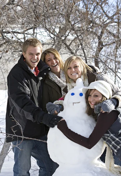 Молодые счастливые люди со снеговиком — стоковое фото