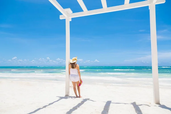 白いペルゴラの下に立っている女性は美しいカリブ海のビーチシーンを見て — ストック写真