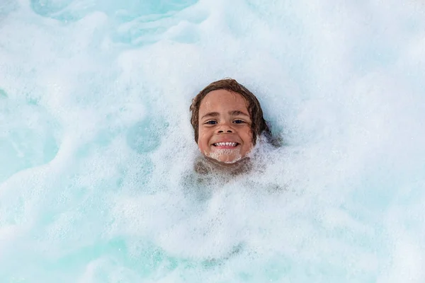 可爱的笑脸男孩在热浴缸或浴缸的泡沫中玩耍 一个可爱的非裔美国男孩在泡沫般的水中嬉戏 开心的表情 — 图库照片