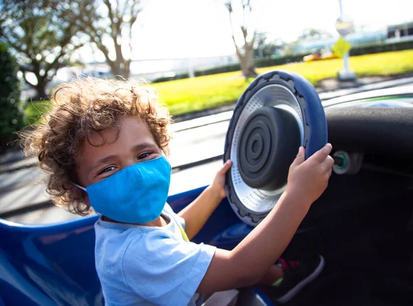 屋外遊園地で楽しいゴーカートに乗る運転かわいいアフリカ系アメリカ人の子供 彼は健康と安全のガイドラインに従うために保護面マスクを着用しています — ストック写真