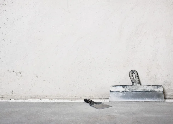 Espátulas de alvenaria perto de uma parede de gesso cinza — Fotografia de Stock