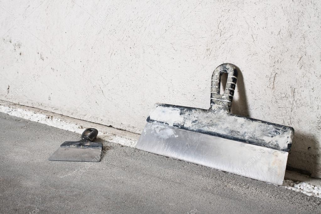 Masonry trowels near a grey plaster wall