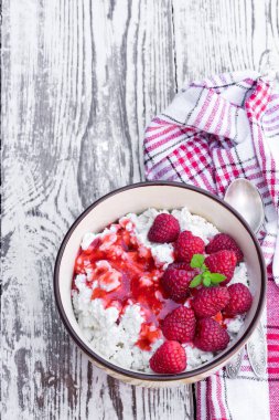 Beyaz ahşap masada seramik kasede ahududulu süzme peynir. 