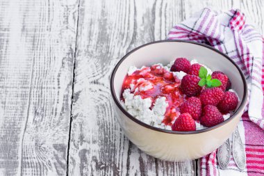 Beyaz ahşap masada seramik kasede ahududulu süzme peynir. 