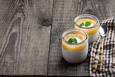 Beyaz kremalı yoğurt, ahşap masada küçük kavanozda sarı meyveli püre. 