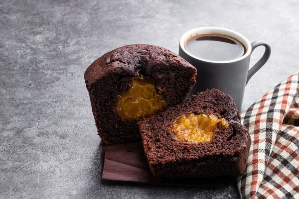 Dark  chocolate muffin stuffed with yellow jam and cup of coffee on gray background