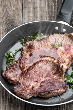 Kızarmış biftek ve ahşap masada tavada otlar. 