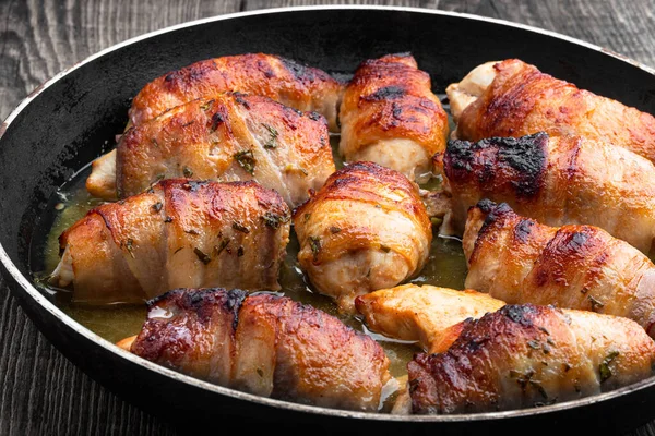 Chicken  breasts wrapped in bacon in frying pan on wooden table