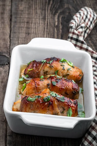 Chicken  breasts wrapped in bacon in white dish on wooden table