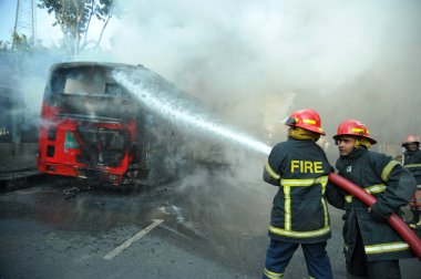Dhaka 'daki yirmi parti ittifakı tarafından 6 Ocak 2015' te uygulanan ülke çapındaki abluka programının ilk gününde muhalefet göstericileri tarafından ateşe verilen yanan araçları itfaiyeciler söndürüyor..