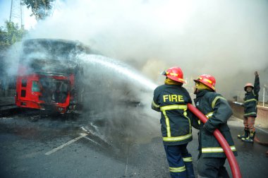 Dhaka 'daki yirmi parti ittifakı tarafından 6 Ocak 2015' te uygulanan ülke çapındaki abluka programının ilk gününde muhalefet göstericileri tarafından ateşe verilen yanan araçları itfaiyeciler söndürüyor..