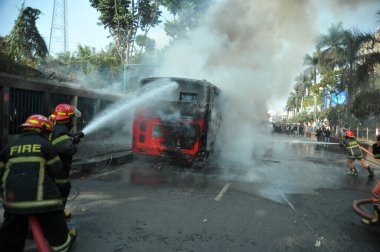 Dhaka 'daki yirmi parti ittifakı tarafından 6 Ocak 2015' te uygulanan ülke çapındaki abluka programının ilk gününde muhalefet göstericileri tarafından ateşe verilen yanan araçları itfaiyeciler söndürüyor..