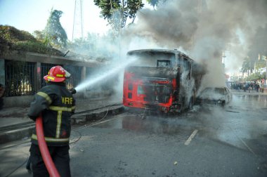 Dhaka 'daki yirmi parti ittifakı tarafından 6 Ocak 2015' te uygulanan ülke çapındaki abluka programının ilk gününde muhalefet göstericileri tarafından ateşe verilen yanan araçları itfaiyeciler söndürüyor..