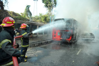 Dhaka 'daki yirmi parti ittifakı tarafından 6 Ocak 2015' te uygulanan ülke çapındaki abluka programının ilk gününde muhalefet göstericileri tarafından ateşe verilen yanan araçları itfaiyeciler söndürüyor..