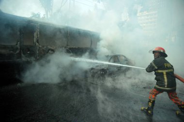 Dhaka 'daki yirmi parti ittifakı tarafından 6 Ocak 2015' te uygulanan ülke çapındaki abluka programının ilk gününde muhalefet göstericileri tarafından ateşe verilen yanan araçları itfaiyeciler söndürüyor..
