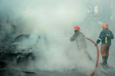 Dhaka 'daki yirmi parti ittifakı tarafından 6 Ocak 2015' te uygulanan ülke çapındaki abluka programının ilk gününde muhalefet göstericileri tarafından ateşe verilen yanan araçları itfaiyeciler söndürüyor..