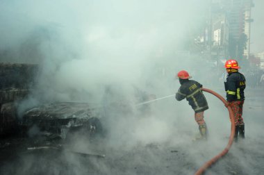 Dhaka 'daki yirmi parti ittifakı tarafından 6 Ocak 2015' te uygulanan ülke çapındaki abluka programının ilk gününde muhalefet göstericileri tarafından ateşe verilen yanan araçları itfaiyeciler söndürüyor..