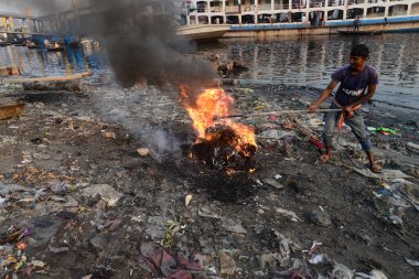 İnsanlar 19 Mart 2022 'de Bangladeş' in Dhaka kentindeki Buriganga Nehri kıyısında çöp yakarak zehirli duman yaratıyor. Dhaka, inşaat, araç emisyonları ve tuğla fırınlarının atıklarıyla dünyanın en kirli şehirlerinden biri olarak sıralamaya devam ediyor.