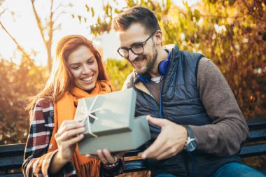 Parkta hediyeleri olan genç bir çift. Adam karısına hediye kutusu veriyor..