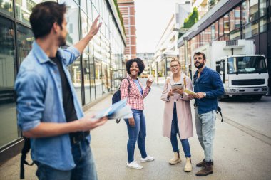 Üniversite ve arkadaşlarının arka planında dururken elinde kitap tutan genç adam.
