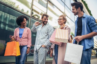 Bir grup arkadaş alışveriş torbalarıyla sokakta yürüyor ve eğleniyorlar..
