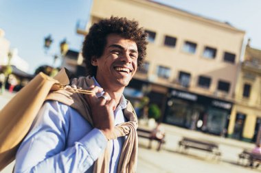 Açık havada alışveriş torbalarıyla gülümseyen karışık ırk adamı..