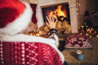 Küçük çocuk elinde lokumlu kakaoyla bir Noel ağacının yanında oturuyor.
