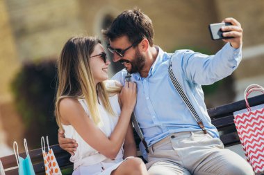 Alışveriş yaptıktan sonra bankta oturan güzel, gülümseyen genç bir çiftin portresi..