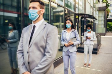 COVID-19 salgını sırasında koruyucu yüz maskeli iş adamları güvenli bir mesafede sırada bekliyorlar..