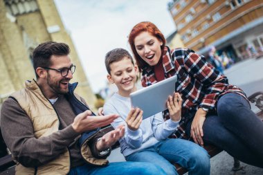 Aile bankta oturuyor, cihaz kullanarak rahatlıyor, internette geziniyor..