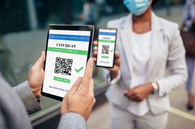Güvenlik maskeli bir iş kadını işverenine elektronik aşı sertifikası gösteriyor.