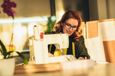 Neşeli genç bayan dikiş dikiyor. Evde çalışıyor..