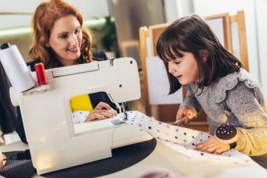 Kızıyla dikiş diken neşeli genç bir kadın. Evde çalışıyor..