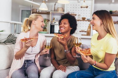 Evdeki kanepede şarap ve pizzayla mutlu genç bayan arkadaşlar.. 