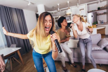 Genç bir kadın evde mikrofona şarkı söyleyerek eğleniyor. Bekarlığa veda partisi, karaoke, müzik konseri ve tatil konsepti 