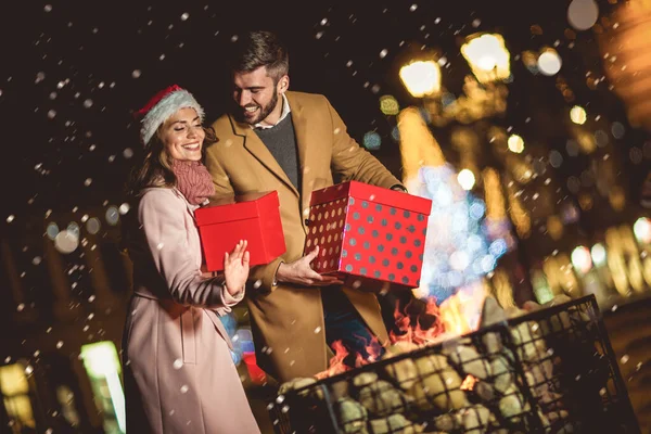 クリスマス前の冬に屋外で楽しいギフトボックスを保持する若いロマンチックなカップル — ストック写真