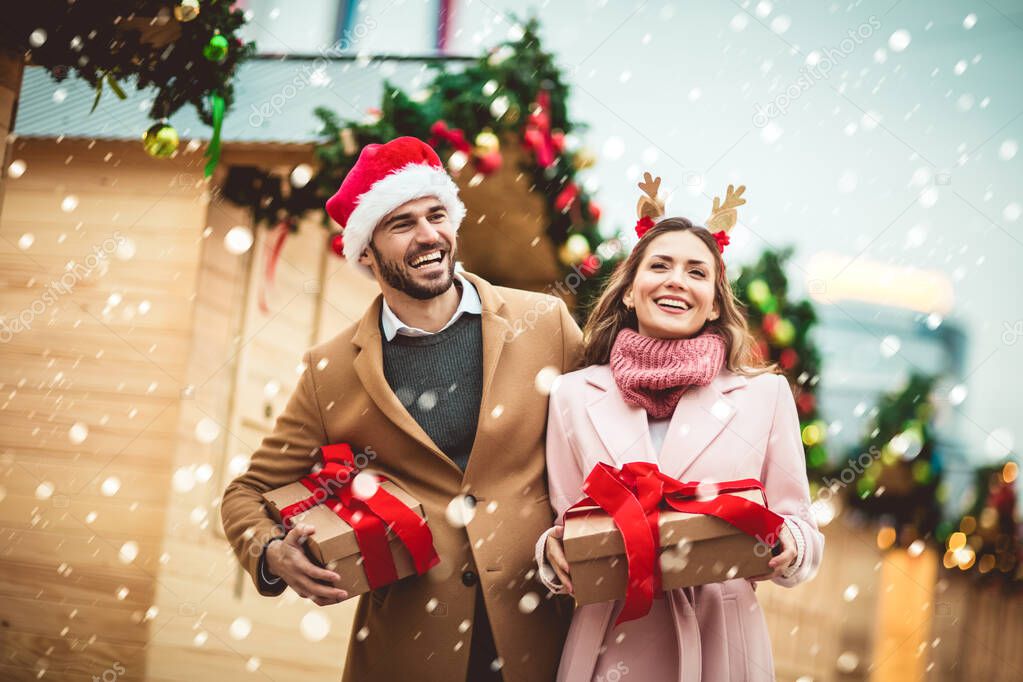 Young romantic couple holding gift box having fun outdoors in winter before Christmas.