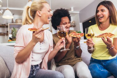 Evdeki kanepede şarap ve pizzayla mutlu genç bayan arkadaşlar.. 
