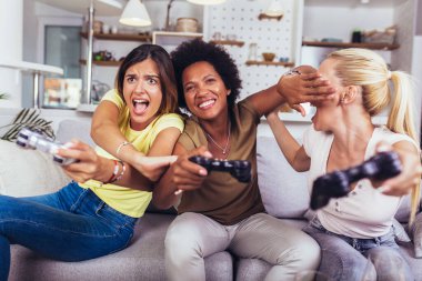 Evde video oyunu oynayan mutlu kadın arkadaşlarının portresi.