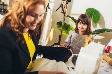 Kızıyla dikiş diken neşeli genç bir kadın. Evde çalışıyor..