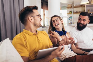 Arkadaşlar evdeki oturma odasındaki koltukta otururken dijital cihazlarını kullanıyorlar.