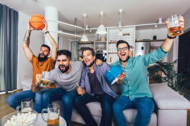 Mutlu erkek arkadaşlar siyah yüz koruyucu maske takıp evde basketbol izliyorlar.