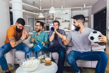 Vuvuzela 'lı mutlu erkek arkadaşlar siyah yüz koruyucu maske takıp evde futbol izliyorlar.