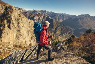 Sırt çantalı gezgin uçurumun kenarında durup dağlara bakıyor. 