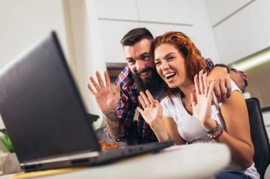 Aşık genç bir çift ev mutfağında şarap içiyor ve dizüstü bilgisayar kullanıyor..