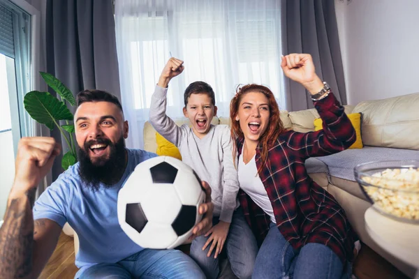 Taraftarların ailesi evde futbol maçı izliyor.