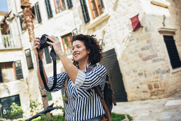 Outdoor summer smiling lifestyle portrait of pretty young woman having fun in the city in Europe in evening with camera travel photo of photographer