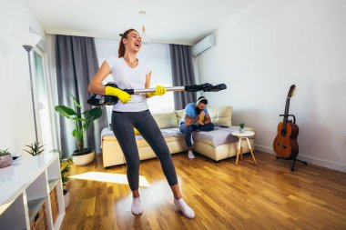 Gülümseyen genç ev hanımı ve kocası elektrik süpürgesiyle eğleniyor.