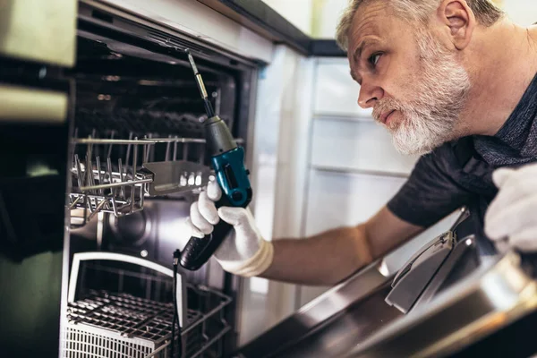 Man with toolbox repairing dishwasher in a household.